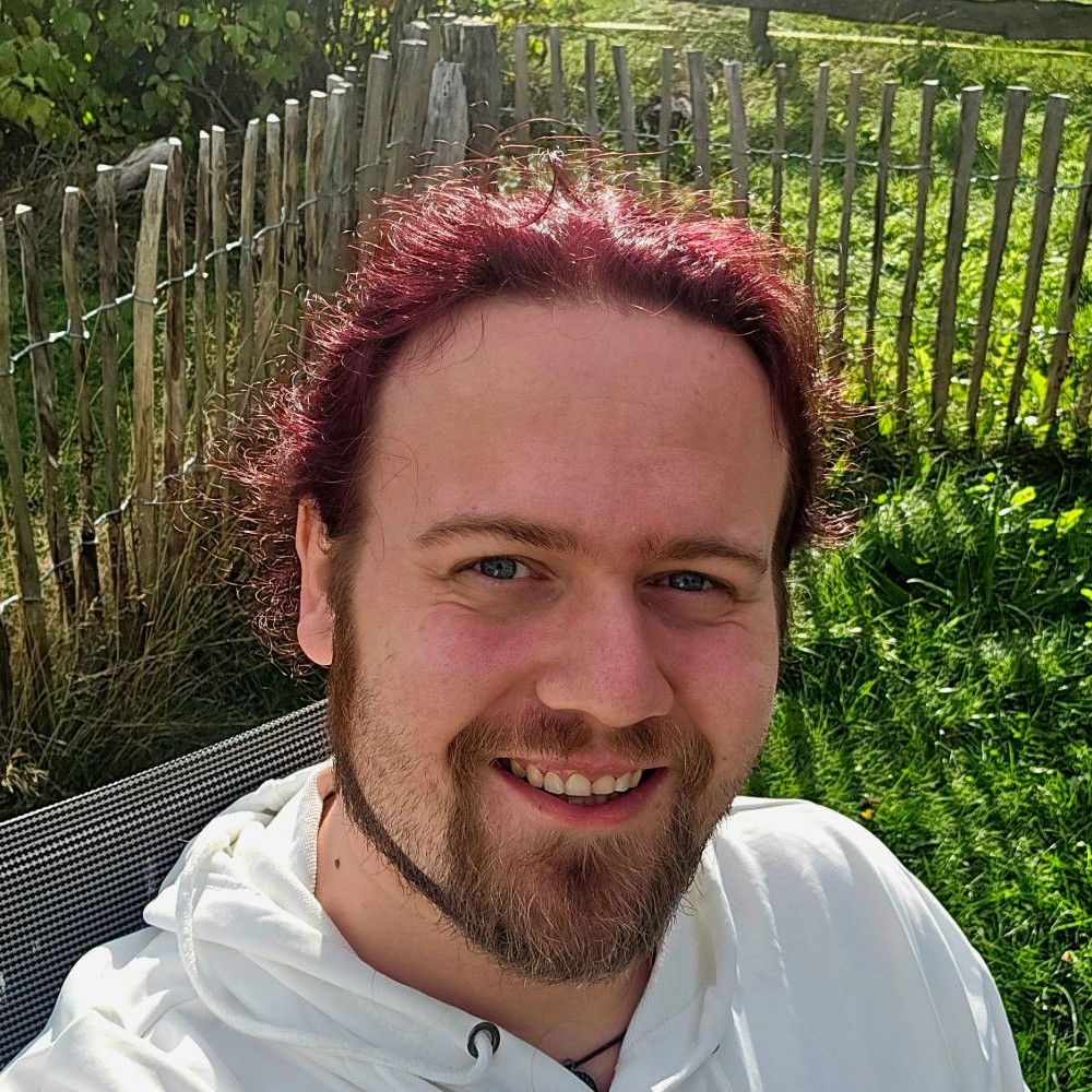 Michael draußen in der Sonne, lachend, vor einem Holzzaun